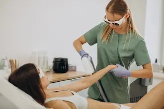 Gözlük takan bir estetisyen, bir kadına buz lazer epilasyon tedavisi uyguluyor.