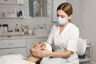 Maske takan bir estetisyen, bir müşterinin yüzüne medikal cilt bakımı uyguluyor.